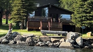 A cabin by a lake with a view of a green mountain range.