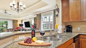 A kitchen with granite countertops, wooden cabinets, a chandelier, and a large window with a view of the outdoors. - First Floor Condo, Near Pools and Attractions (Kissimmee)