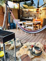 Una terraza de madera con una parrilla, una hamaca y una mesa con sillas.