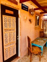 Una puerta de madera con tallas intrincadas, un letrero encima y una mesa con una silla frente a un edificio de pared con textura.