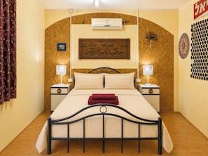 Habitación de hotel con cama, dos mesitas de noche, aire acondicionado de pared, un adorno en la pared y cortina estampada.