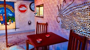 A rustic outdoor seating area with a table and chairs, a mural with a stop sign, a clock, and a window.