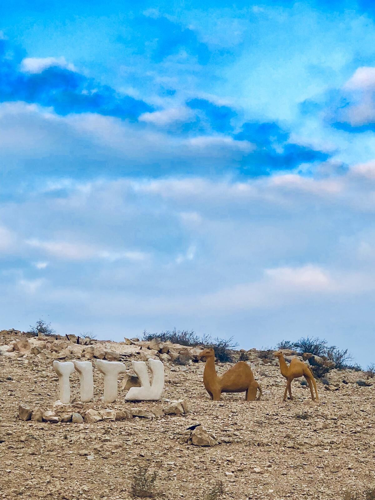 A desert landscape with two camels and a large white structure.