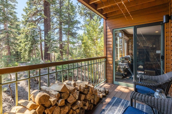 A wooden deck with a railing, a stack of firewood, and a wicker chair.