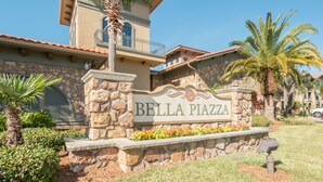 Señal de Bella Piazza con fachada de piedra, balcón y área ajardinada con plantas y flores.