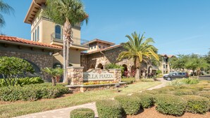 Un edificio residencial con fachada de piedra, un letrero que dice "Bella Piazza" y un césped bien cuidado con varios arbustos.