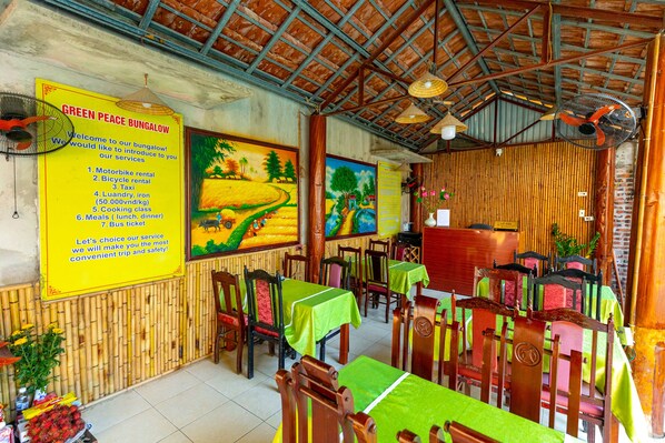 Un restaurante con paredes de bambú, manteles verdes y sillas de madera.