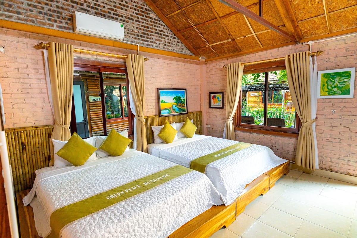 A room with two beds, a brick wall, a wooden ceiling, and a window with curtains.
