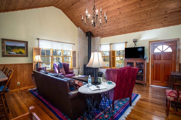 A cozy living room with a wooden ceiling, a fireplace, a television, and a dining area with wooden furniture.