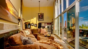 A spacious living area with a large sofa set, a fireplace, and a large window offering a view of the outdoors. - MT. SOLEDAD BEACH PARADISE - AMAZING PANORAMIC VIEWS! - HEATED POOL & JACUZZI (San Diego)