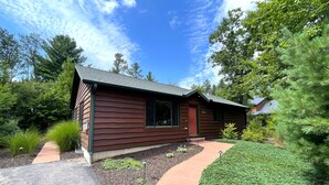 A single-story wooden house with a red door, surrounded by a landscaped garden with various plants and a paved driveway. - Dogwood Dream @ Spring Brook Resort (Wisconsin Dells)