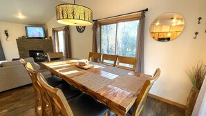A dining area with a wooden table, chairs, a chandelier, a fireplace, and a television in the background. - Dogwood Dream @ Spring Brook Resort (Wisconsin Dells)