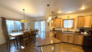A spacious kitchen with wooden cabinets, a granite countertop, and a dining area with a table and chairs. - Dogwood Dream @ Spring Brook Resort (Wisconsin Dells)