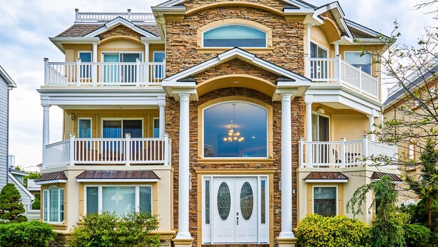 A two-story house with a stone facade, white balconies, and a large arched window.