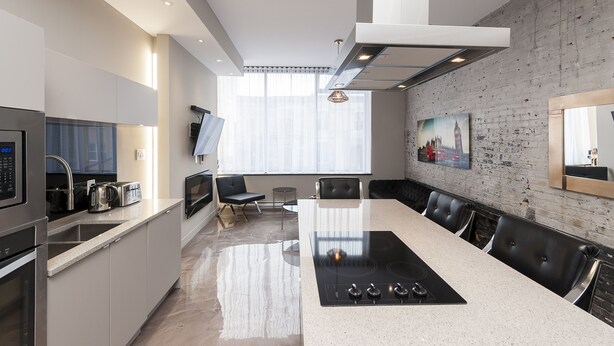 A modern kitchen with a central island, stainless steel appliances, and a dining area with leather chairs. - Modern Suite: Steps from Place des Arts (Montreal)