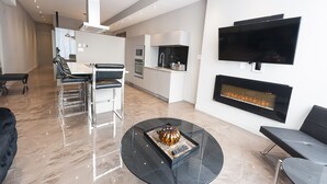 A modern living room with a fireplace, a flat-screen TV, and a dining area with a kitchen in the background. - Modern Suite: Steps from Place des Arts (Montreal)