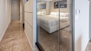 A modern bedroom with a glass partition, a bed, a nightstand, and a cityscape painting on the wall. - Modern Suite: Steps from Place des Arts (Montreal)