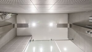 A modern, minimalist bathroom with a geometric patterned ceiling, a large mirror, and a glass shower enclosure. - Modern Suite: Steps from Place des Arts (Montreal)