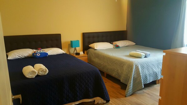 Two single beds with dark headboards, a bedside table with a lamp, and a wooden dresser.