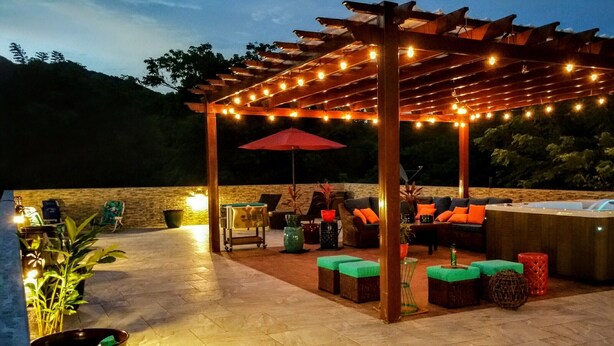 Eine Terrasse im Freien mit einer Holz-Pergola, Lichterketten und einem Whirlpool.
