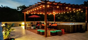 An outdoor patio with a wooden pergola, string lights, and a hot tub.