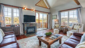 A spacious living room with a fireplace, leather sofas, a coffee table, and large windows offering mountain views. - Mountain Views, Steps from the Lifts (Big Sky)