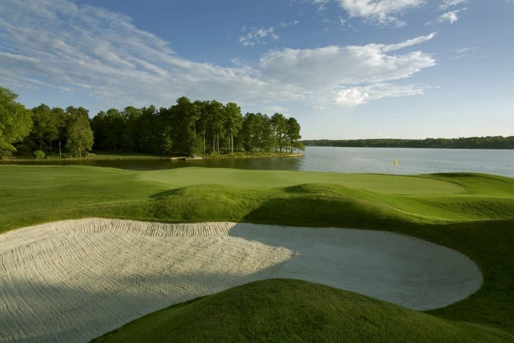 Un parcours de golf avec des bunkers de sable, des obstacles d’eau et une zone boisée en arrière-plan.