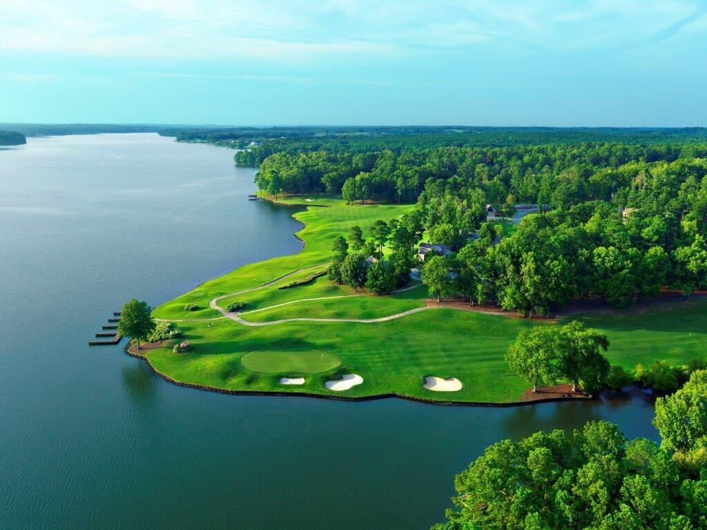 Vue aérienne d’un terrain de golf avec un plan d’eau, entouré d’une végétation luxuriante et de quelques bâtiments.