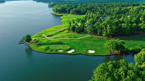 An aerial view of a golf course with a water body, surrounded by dense greenery and a few buildings. - Spacious Family-Friendly Retreat w/ Winter Rates! (Greensboro)