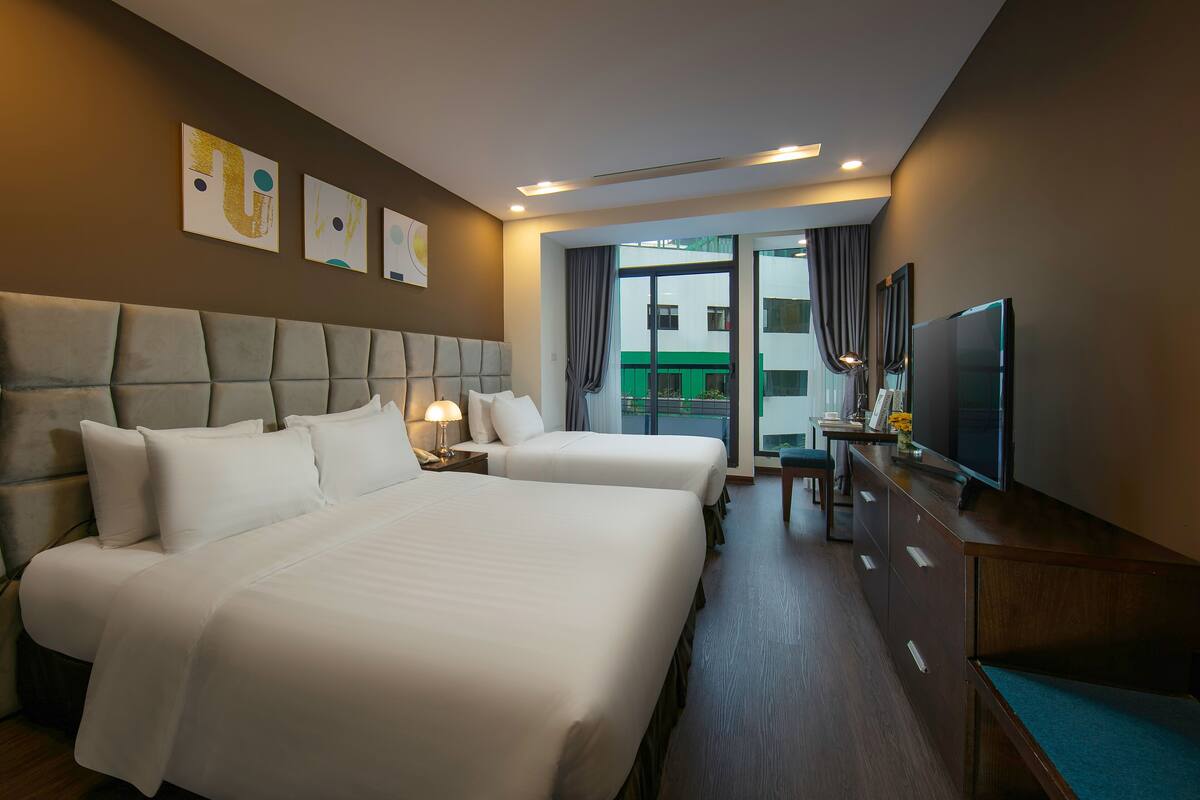 A hotel room with two beds, a TV, a desk, and a view of the outside.