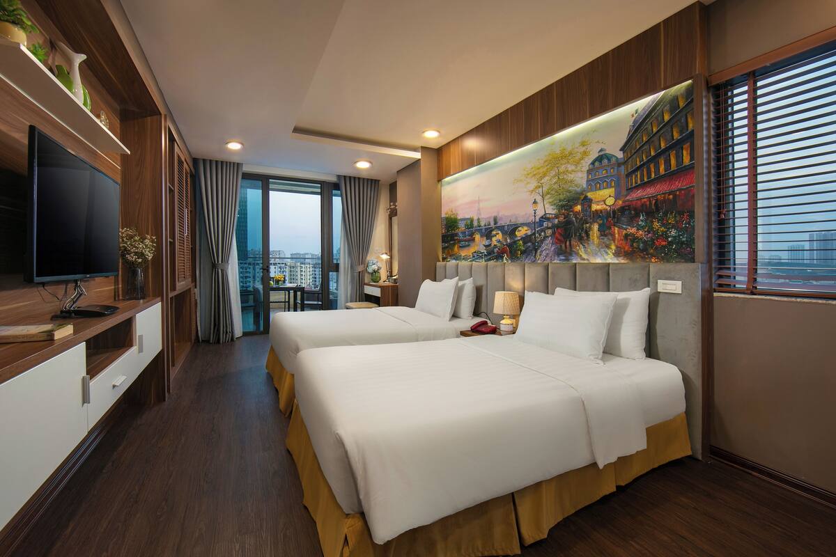 A hotel room with two beds, a TV, a painting, and a city view.