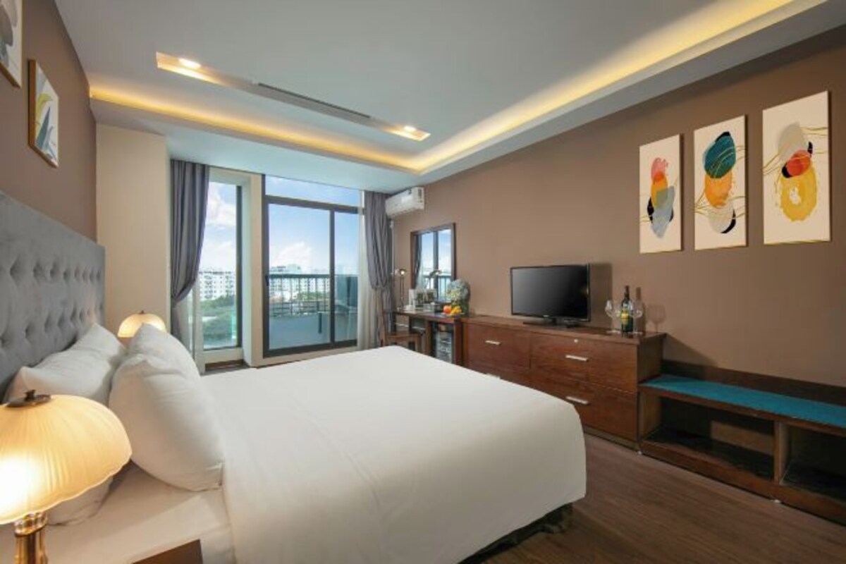 Ein modernes Hotelzimmer mit einem großen Bett, einem Fernseher, einem Schreibtisch und einem Balkon mit Blick auf die Stadt.