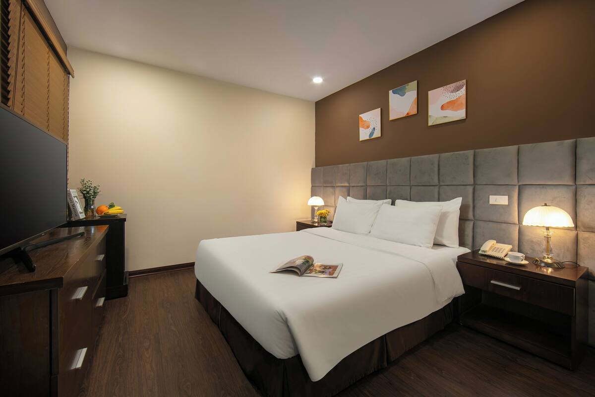 A hotel room with a large bed, bedside tables, a desk, and a TV.
