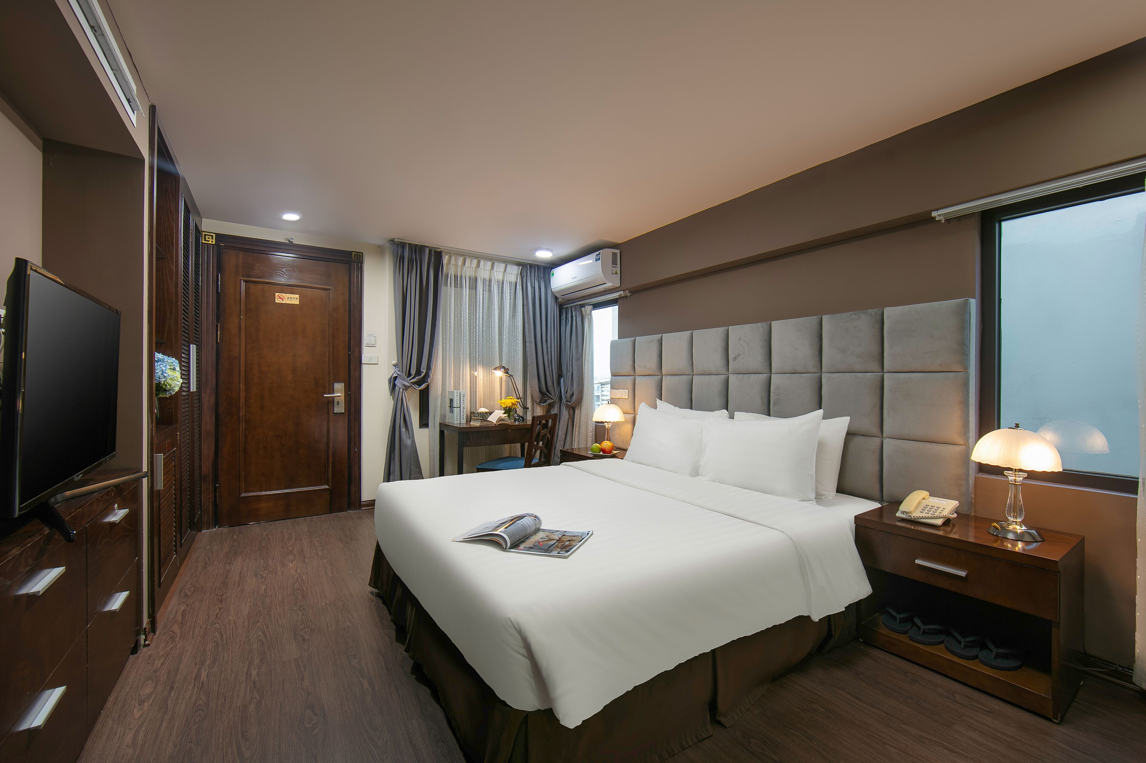 A hotel room with a large bed, a bedside table with a lamp, a TV, and a wardrobe.