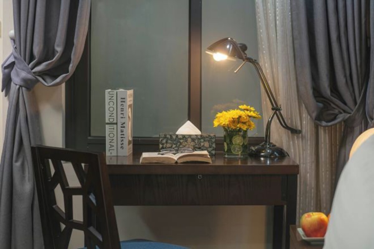 Ein Schreibtisch mit einer Lampe, einem Buch mit dem Titel 'Unconditional' und einer Vase mit gelben Blumen.