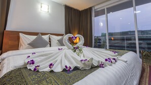 A hotel room with a large bed, a heart-shaped towel arrangement, and a view of the cityscape through the window. - Villa Bayon Guides (Siem Reap)
