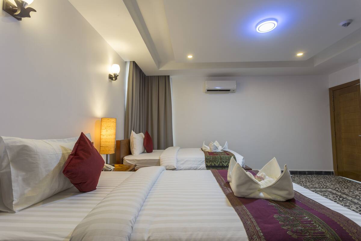 A hotel room with two beds, a sitting area, an air conditioning unit, and a patterned rug.