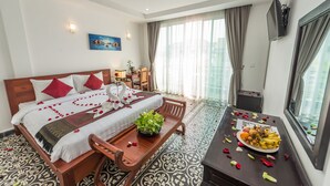 A hotel room with a bed, a dining table with a plate of food, a TV, and a window with curtains. - Villa Bayon Guides (Siem Reap)