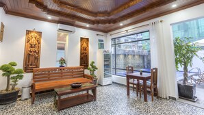 A room with a wooden bench, a dining table, and chairs. There are potted plants and a refrigerator. - Villa Bayon Guides (Siem Reap)