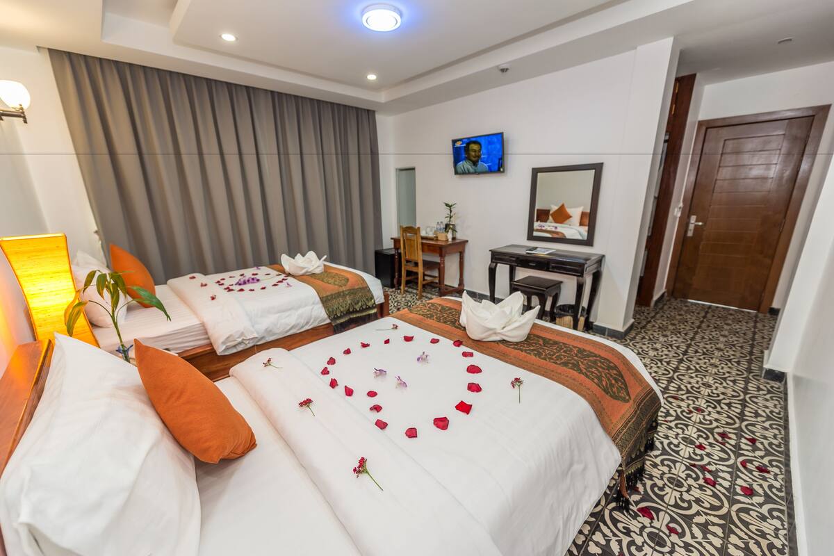 A hotel room with two beds, a desk, a chair, a television, and a mirror.
