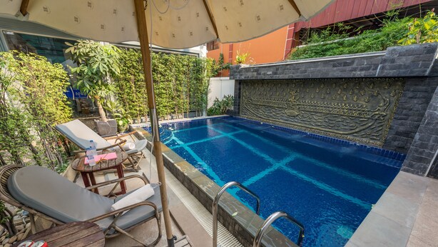 A swimming pool with lounge chairs and a table, surrounded by plants and a decorative wall. - Villa Bayon Guides (Siem Reap)