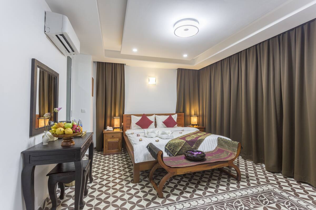 A hotel room with a bed, bedside tables, a desk with a chair, a mirror, and a patterned floor.