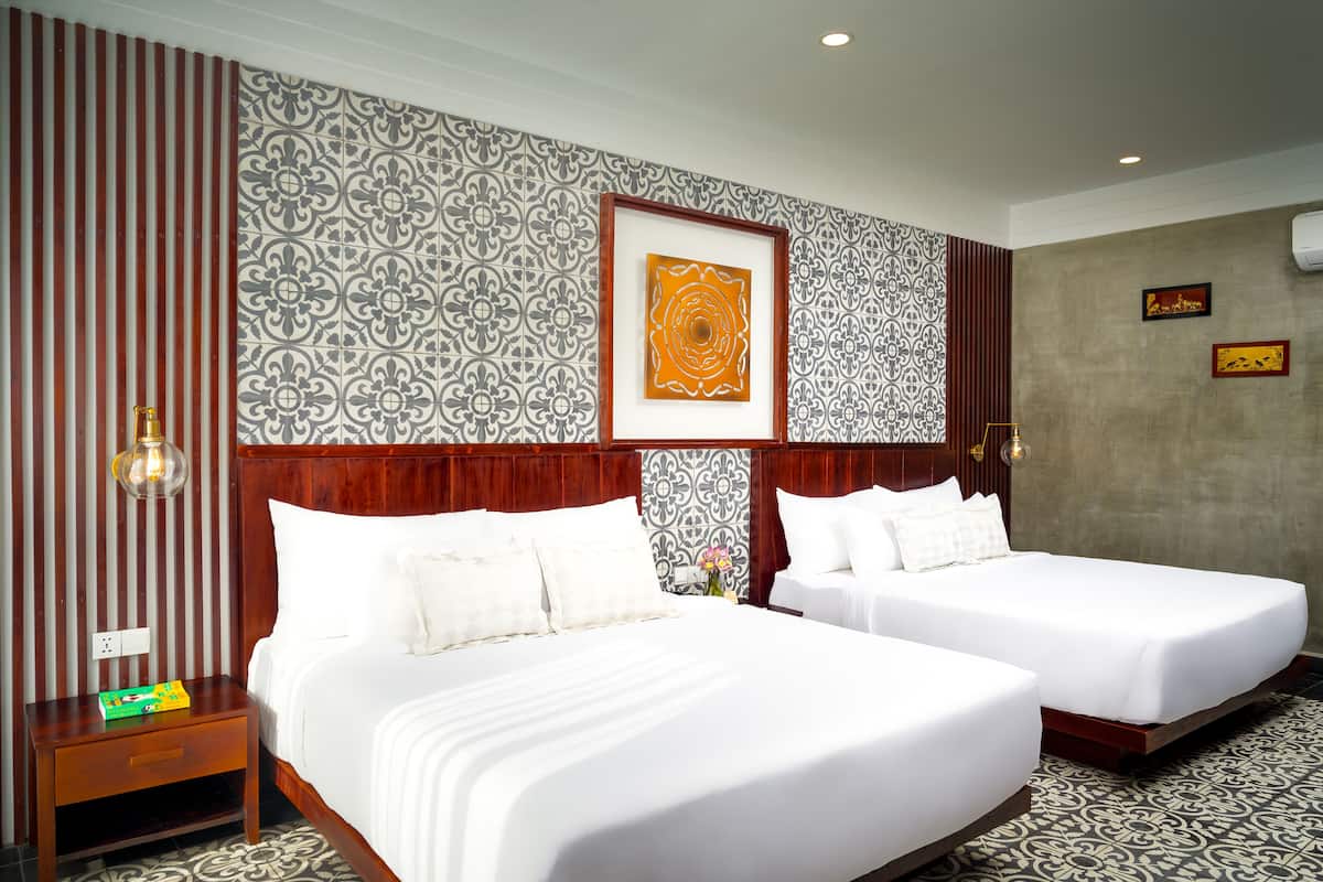 A hotel room with two beds, a nightstand, a wall with patterned wallpaper, and a framed artwork.