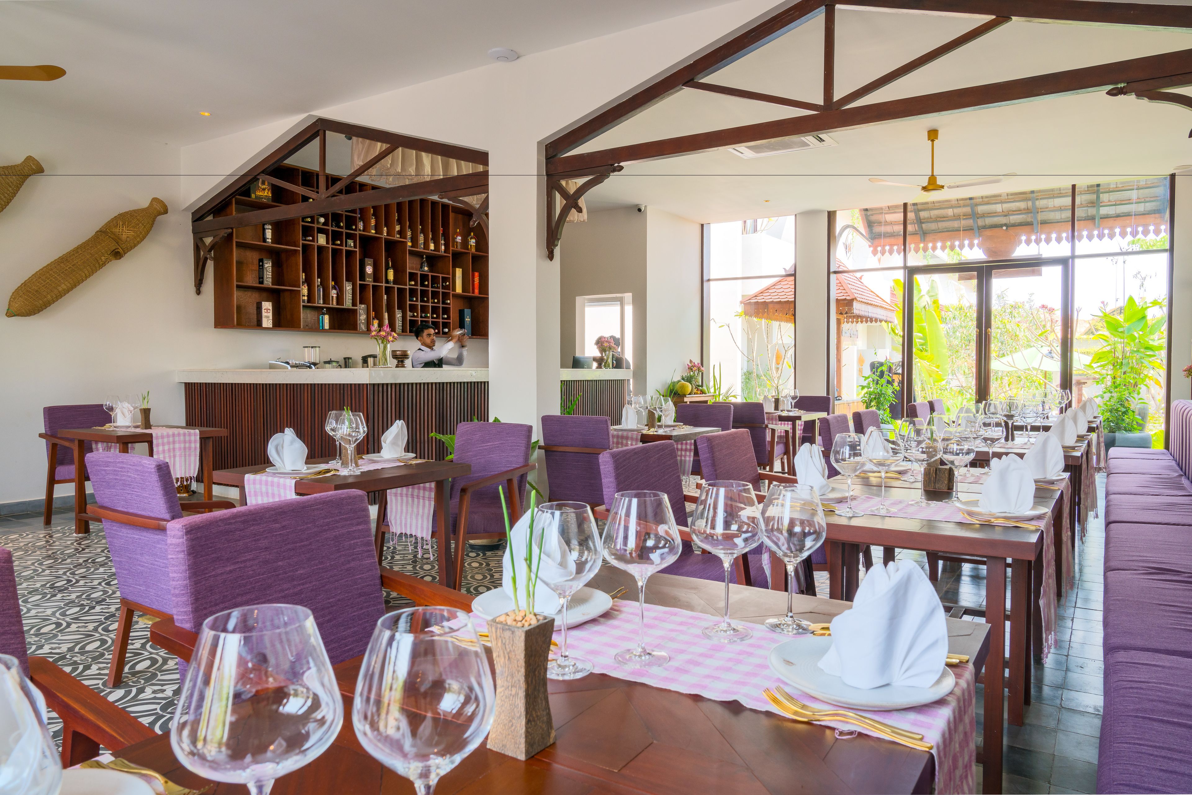 A restaurant with purple upholstered chairs, wooden tables, and a bar area with shelves of bottles.