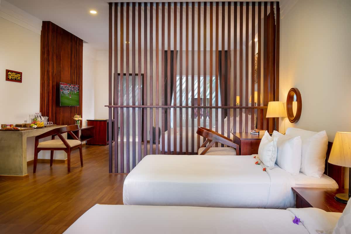 A hotel room with a wooden desk, a television, a bed with white linens, and a decorative partition.