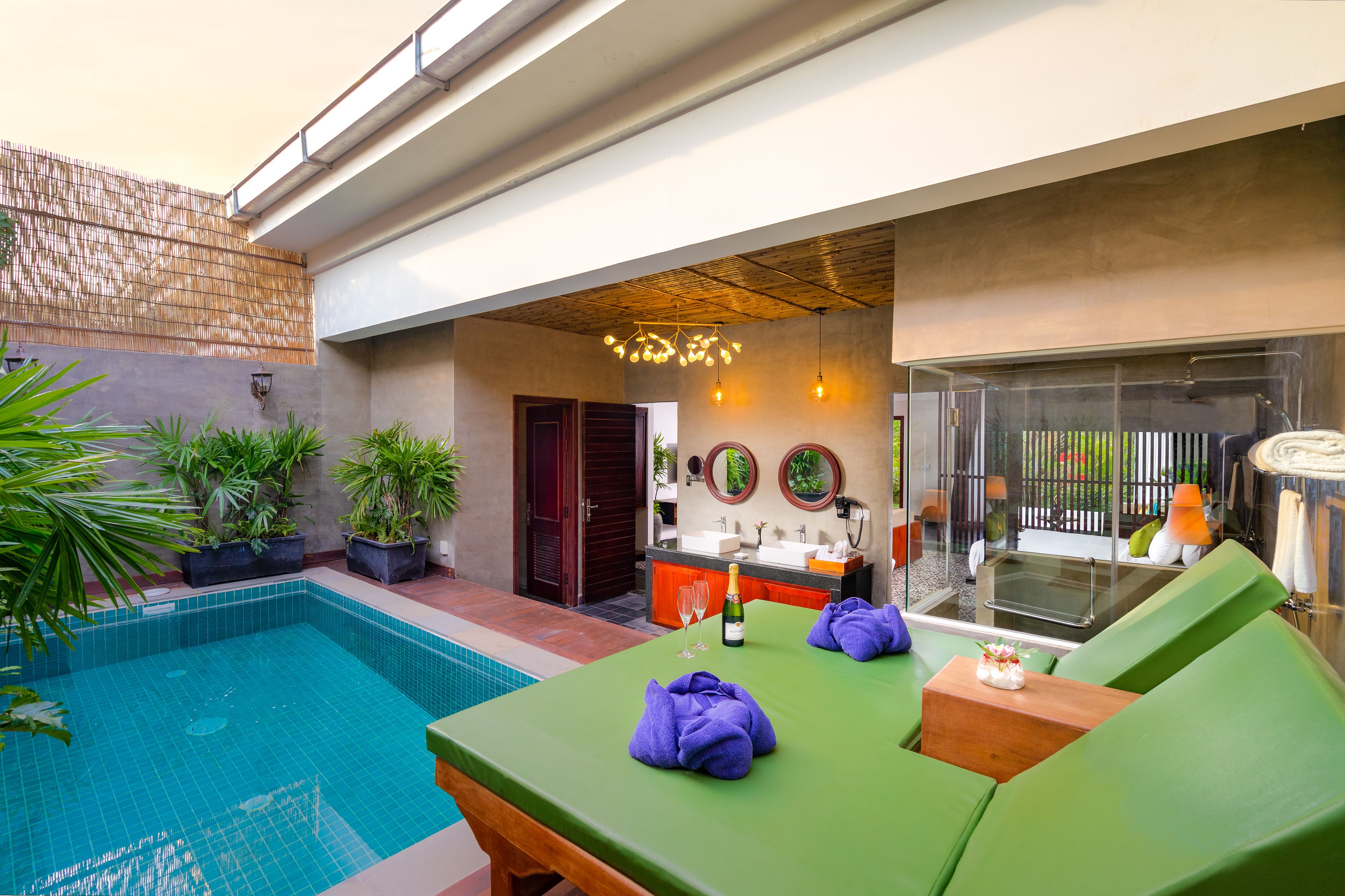 A poolside area with a green lounge chair, a table with a bottle and glasses, and a bar area with a sink and mirror.