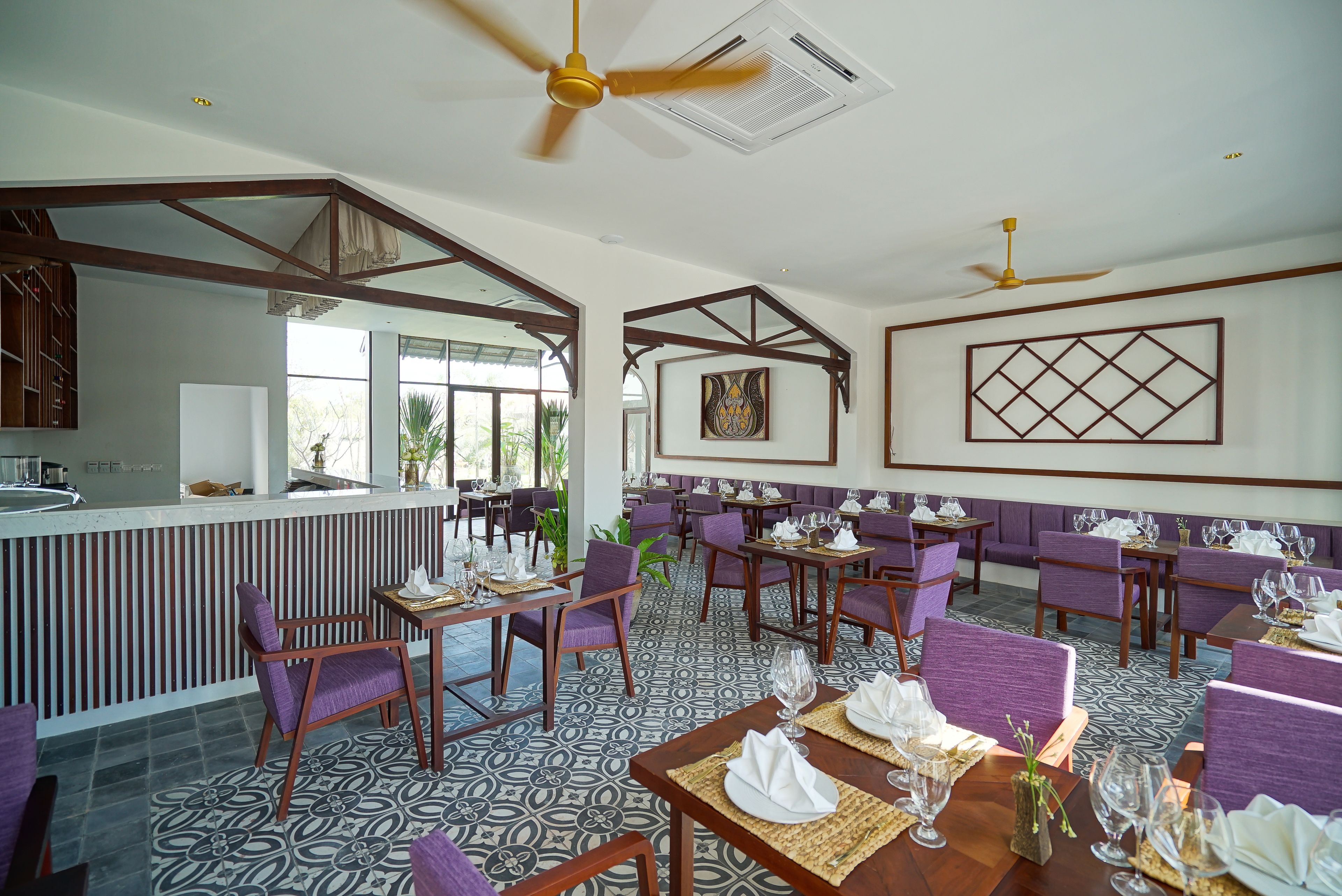 A restaurant with a bar area, purple upholstered chairs, and patterned floor tiles.