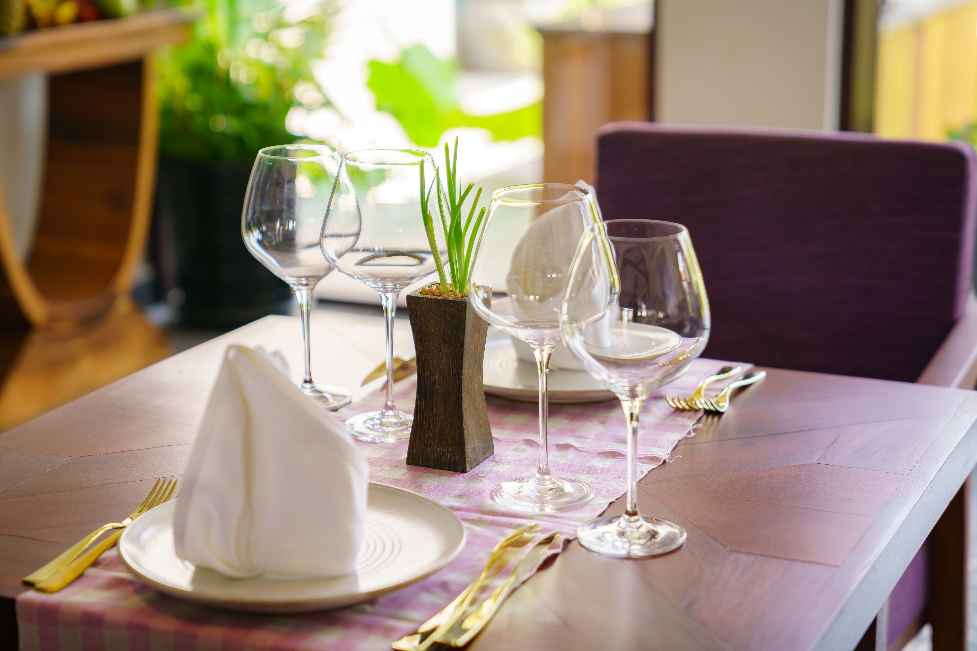 A dining table set with white plates, clear wine glasses, and gold cutlery on a checkered tablecloth.