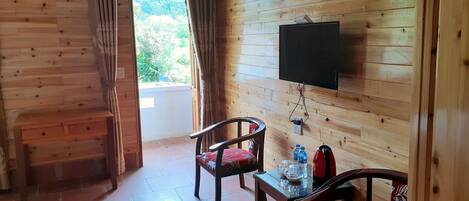 A wooden-paneled room with a television mounted on the wall, a table with chairs, and a view of greenery outside.