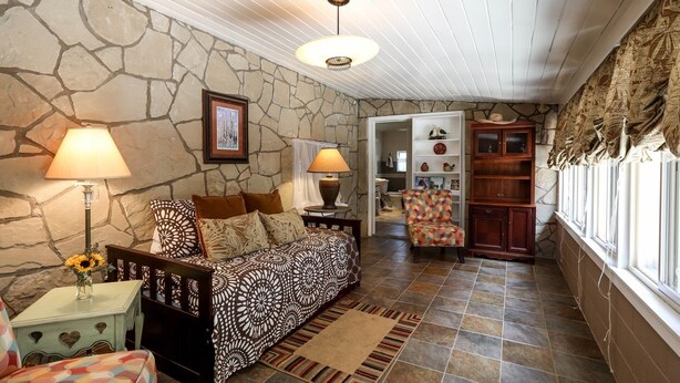 A cozy living room with a stone wall, a patterned sofa, two lamps, and a bookshelf. - Sam Houston's Retreat | Walking distance to Festivals | Close to Main Street (Fredricksburg)
